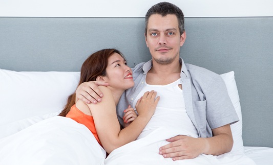 Close-up of a smiling couple embracing and lying in bed. Man is happy looking at camera.